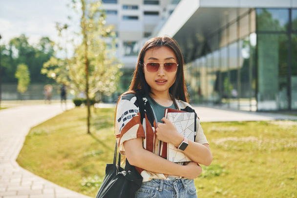 With notepad in hands. Young asian woman is outdoors at daytime. - Fotografie, Obrázek