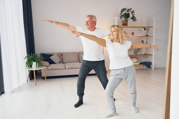Sportive exercises. Senior man and woman is together at home. - Valokuva, kuva