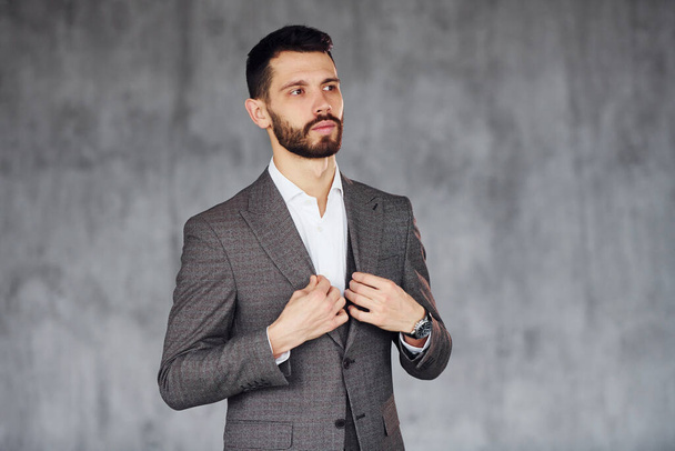 Standing against grey background. Young stylish businessman in suit indoors. Conception of success. - 写真・画像