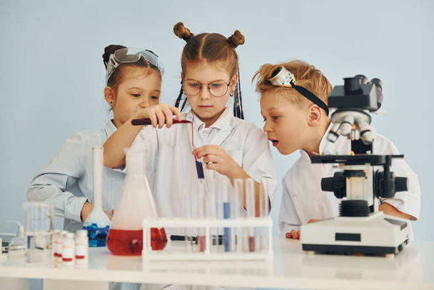 Tubos de ensayo con líquido colorido. Niños con batas blancas interpretan a un científico en el laboratorio usando equipo. - Foto, imagen