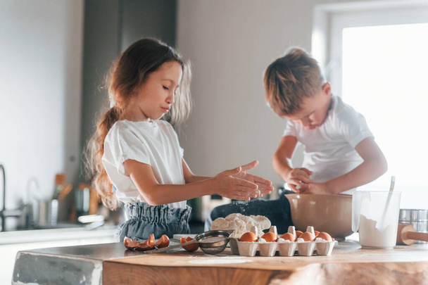 Sitting on the table. Little boy and girl preparing Christmas cookies on the kitchen. - Foto, Imagem