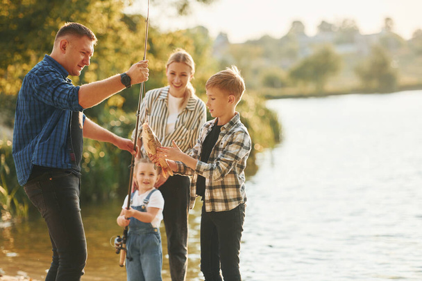 Weekend activities. Father and mother with son and daughter on fishing together outdoors at summertime. - Foto, imagen