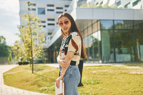 With notepad in hands. Young asian woman is outdoors at daytime. - Fotoğraf, Görsel