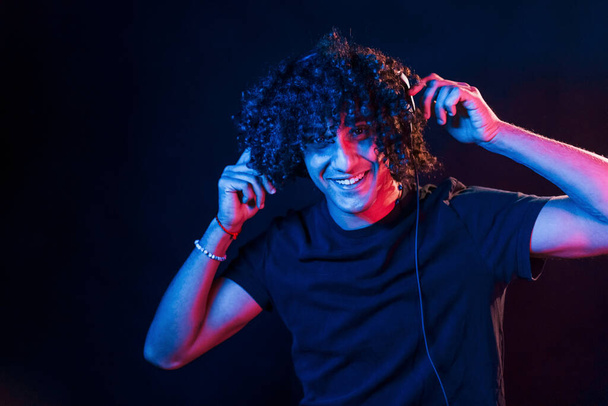 Young DJ with curly hair standing in the club with neon light. - Photo, Image