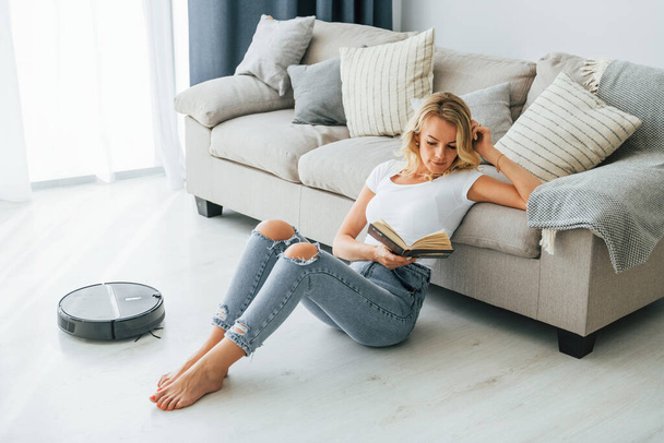 Blonde sits on the floor. Woman in casual clothes is indoors at home. - Foto, Imagem