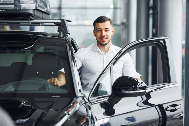 Young man in white shirt is indoors with modern new automobile. - Foto, Bild