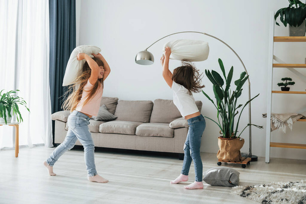 Girls are playing pillow fight game. Kids having fun in the domestic room at daytime together. - Foto, afbeelding