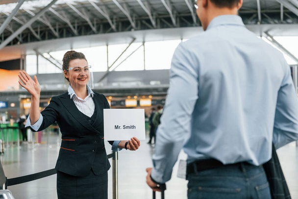 Meet by the woman with text. Young businessman in formal clothes is in the airport at daytime. - Fotografie, Obrázek