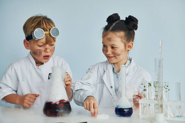 Boy works with liquid in test tubes. Children in white coats plays a scientists in lab by using equipment. - Фото, зображення