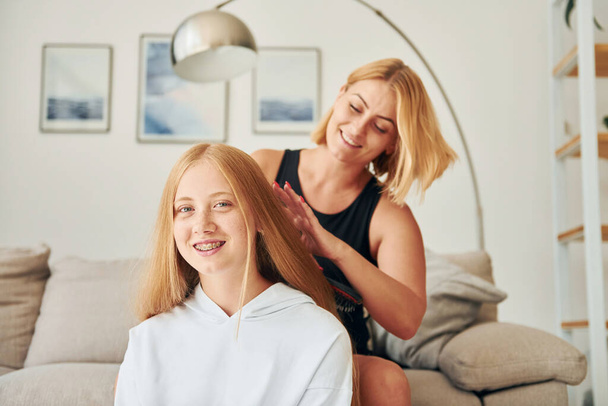 Parent helping with hair. Female teenager with her mother is at home at daytime. - Фото, изображение