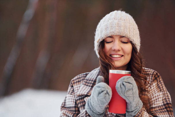 Beautiful woman in warm clothes have a walk in the winter forest. With drink. - Photo, Image