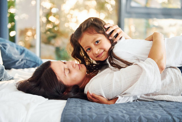 Lying down on the bed. Mother and her daughter spending time together at home. - Foto, imagen