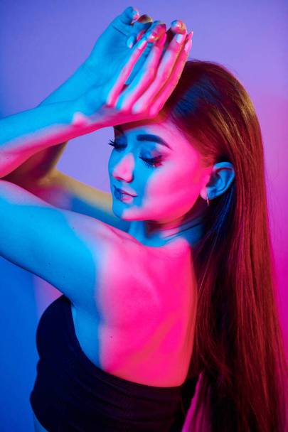 Posing with hands up. Fashionable young woman standing in the studio with neon light. - Photo, image