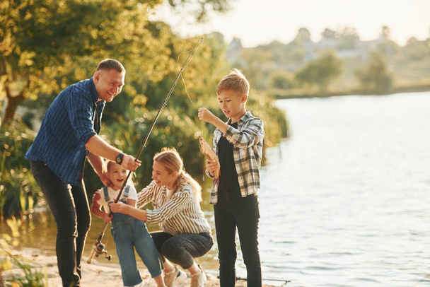 At summertime. Father and mother with son and daughter on fishing together outdoors. - Foto, imagen