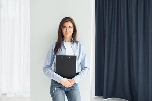Young woman in glasses, formal clothes and with notepad standing indoors. - Foto, immagini
