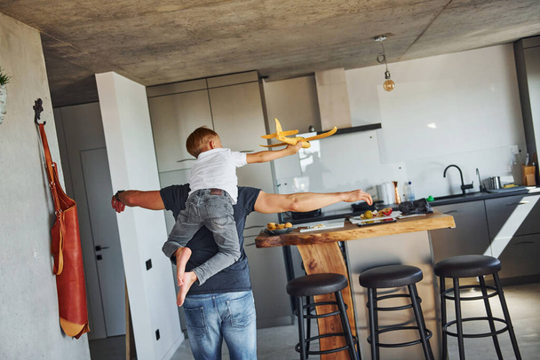 Playing with yellow toy plane. Father and son is indoors at home together. - Fotoğraf, Görsel