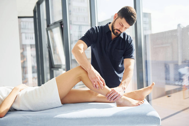 Guy does legs massage. Young woman is lying down when man serves her at spa. - Photo, Image