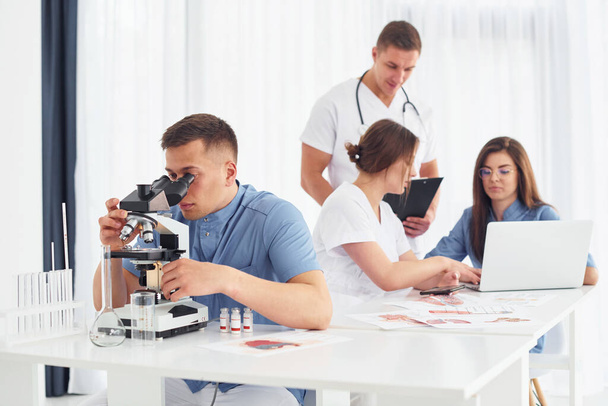 Using microscope. Group of young doctors is working together in the modern office. - 写真・画像