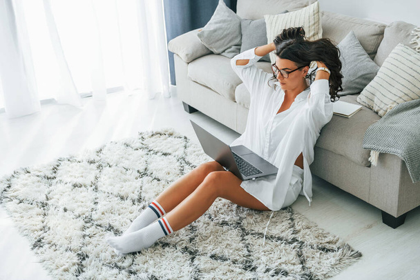 Uses laptop. Woman in casual clothes is indoors at home. - Foto, Imagen