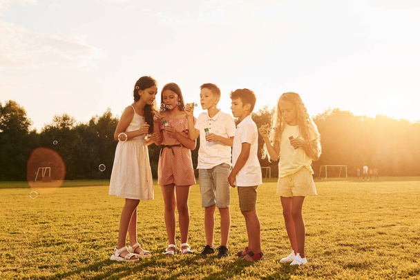 Illuminated by sunlight. Standing on the sportive field. Group of happy kids is outdoors at daytime. - Foto, Imagem