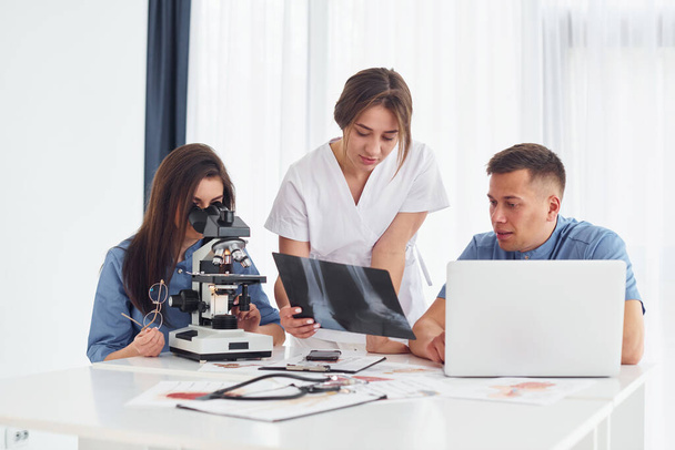 Usando microscopio. Grupo de médicos jóvenes está trabajando juntos en la oficina moderna. - Foto, Imagen