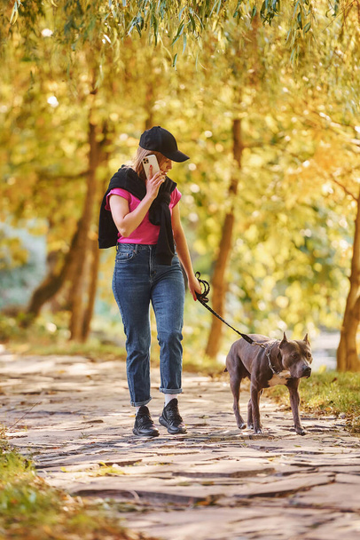 Having fun. Woman in casual clothes is with pit bull outdoors. - Фото, изображение