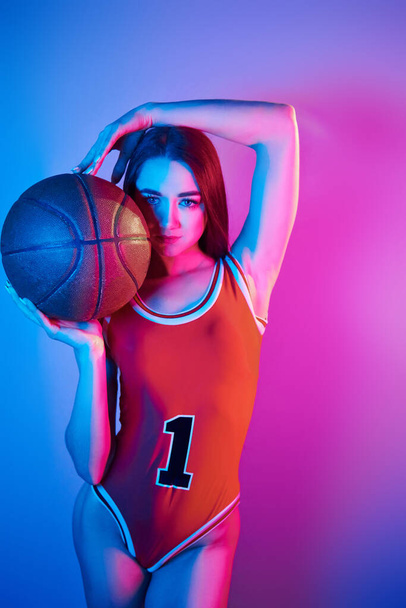 In basketball uniform. Fashionable young woman standing in the studio with neon light. - Φωτογραφία, εικόνα