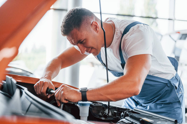 Man in uniform is repairing broken automobile indoors. - Valokuva, kuva