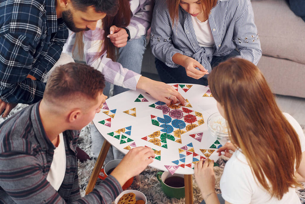 Focused at puzzle game. Group of friends have party indoors together. - Foto, immagini
