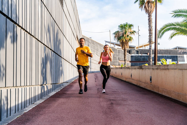 Interracial sportive couple running outdoors - Multiracial couple of runners wearing sportswear and doing functional workout outdoors to strenght body muscles, core abs, stamina and cardio - Foto, afbeelding