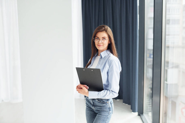 Young woman in glasses, formal clothes and with notepad standing indoors. - Foto, Bild
