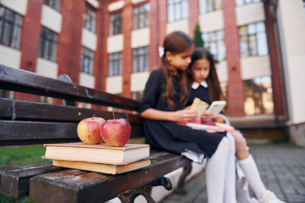 Books and apples. Two schoolgirls is outside together near school building. - Foto, imagen