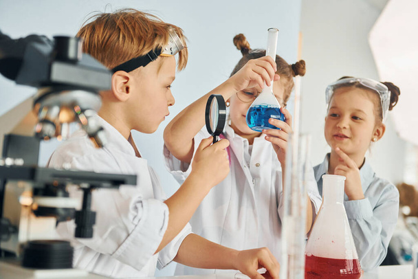 Standing by the table with test tubes. Children in white coats plays a scientists in lab by using equipment. - Foto, Imagem