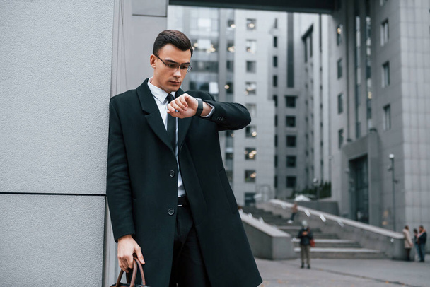 Standing near the building. Businessman in black suit and tie is outdoors in the city. - Foto, imagen