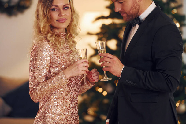 Standing against christmas tree. Happy couple have a new year party indoors together. - Foto, immagini