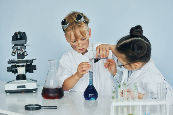 Little girl and boy in white coats plays a scientists in lab by using equipment. - Foto, imagen