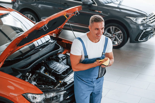 Professional service. Man in uniform is repairing broken automobile indoors. - Фото, зображення