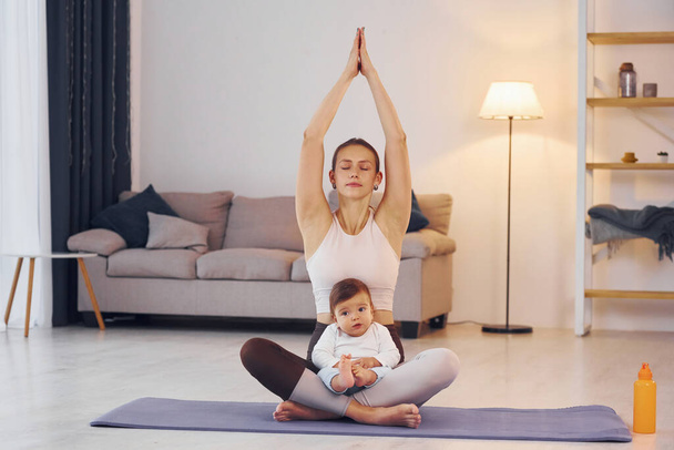 On the yoga mat. Mother with her little daughter is at home together. - Photo, image