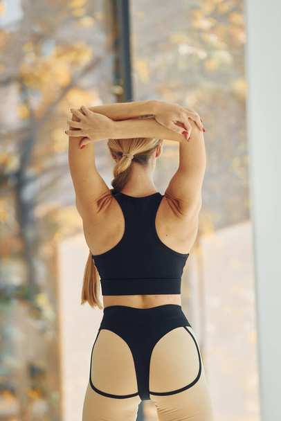 Standing against window. Woman in sportive clothes doing yoga indoors. - Foto, Bild