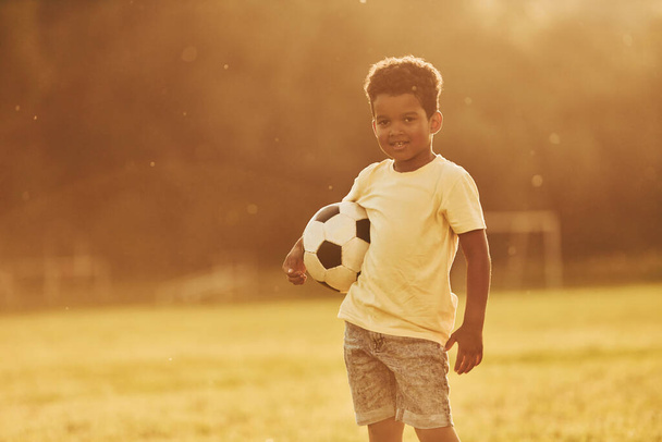 Illuminated by sunlight. African american kid have fun in the field at summer daytime. - Foto, afbeelding