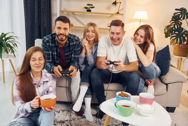 Using joysticks to play video game. Group of friends have party indoors together. - Foto, Imagem
