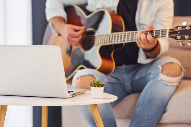 Making a song. Man in casual clothes and with acoustic guitar is indoors. - Foto, imagen