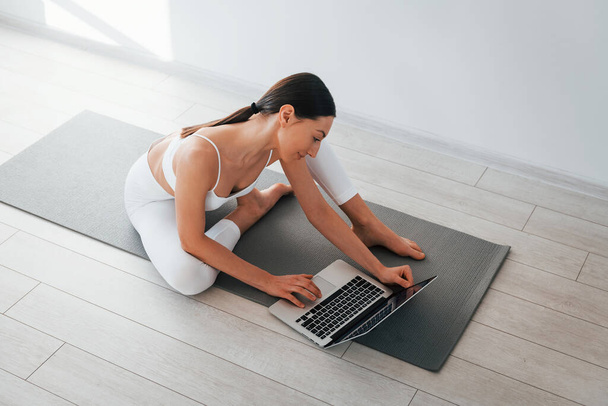 On yoga mat. Young caucasian woman with slim body shape is indoors at daytime. - Foto, Bild