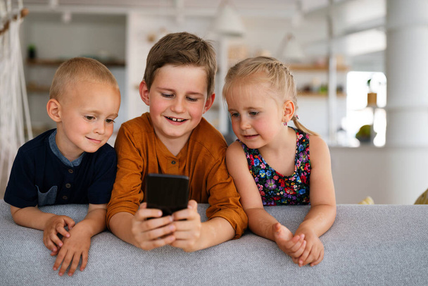Portrait of children having fun, playing on mobile phone together at home. Internet and network addiction. - Fotó, kép
