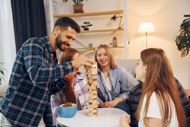 Wooden tower game on the table. Group of friends have party indoors together. - Photo, Image