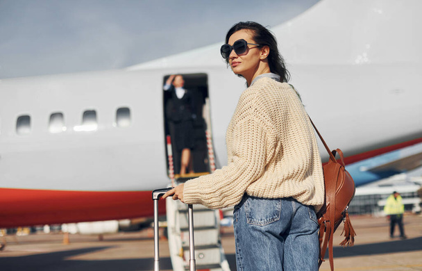 At daytime. Young female passanger in casual clothes is outdoors near the plane. - Foto, Imagem