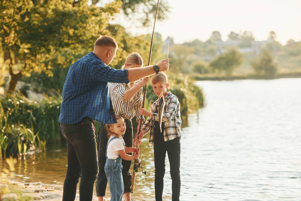 Hétvégi tevékenységek. Apa és anya fiával és lányával együtt horgásznak a szabadban nyáron.. - Fotó, kép