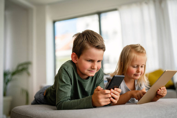Little girl and boy watching video or playing games on their digital device tablet, smartphone. Children digital addiction concept. - Foto, Imagem
