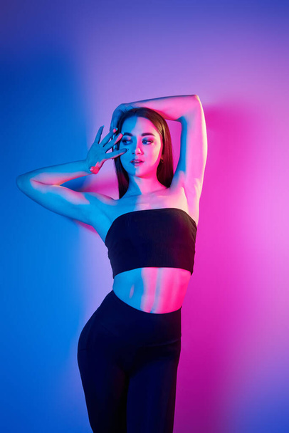 In black clothes. Fashionable young woman standing in the studio with neon light. - Foto, Imagen