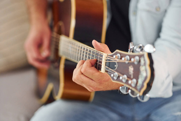 Close up view. Man in casual clothes and with acoustic guitar is indoors. - Photo, Image